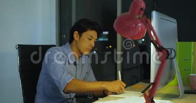 年轻的亚洲艺术家坐在办公室里，画着一支数字笔。 在深夜。